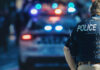 Police officer stands near patrol car with lights flashing