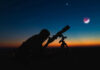 Silhouette of person using telescope against colorful twilight sky