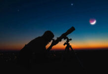 Silhouette of person using telescope against colorful twilight sky