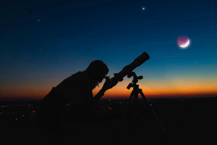 shutterstock_1715179471.jpg Silhouette of person using telescope against colorful twilight sky