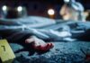 Crime scene with covered body and hand exposed.