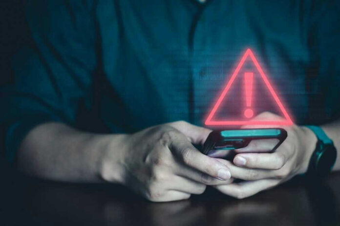 shutterstock_2342619545.jpg Person Holding Phone with Warning Symbol
