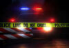 Police car with flashing lights behind caution tape