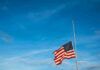 American flag at half-mast against a clear blue sky