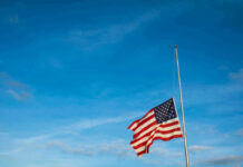 American flag at half-mast against a clear blue sky