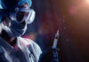 Person in PPE holding syringe with liquid droplets