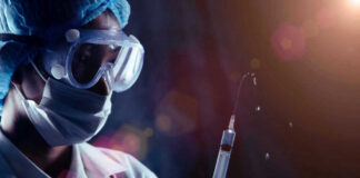 Person in PPE holding syringe with liquid droplets