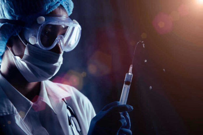Person in PPE holding syringe with liquid droplets