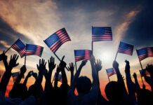 Silhouetted crowd holding American flags against a sunset