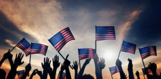 Silhouetted crowd holding American flags against a sunset