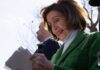 Nancy Pelosi smiling while holding papers outdoors
