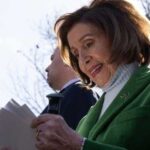 Nancy Pelosi smiling while holding papers outdoors