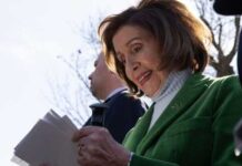 Nancy Pelosi smiling while holding papers outdoors