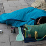 Person sleeping on pavement in a blue sleeping bag