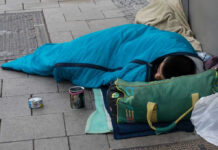 Person sleeping on pavement in a blue sleeping bag
