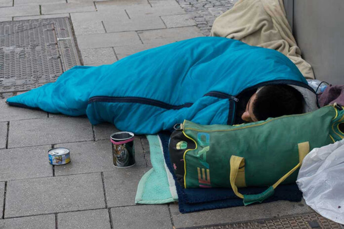 1170197935 Person sleeping on pavement in a blue sleeping bag