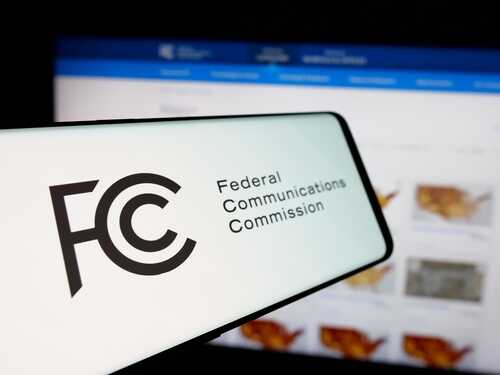 Close-up of a mobile device displaying the FCC logo with a website in the background