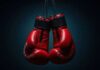 A pair of red boxing gloves hanging against a dark background