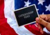 Hand holding a card that reads CITIZENSHIP TEST in front of an American flag