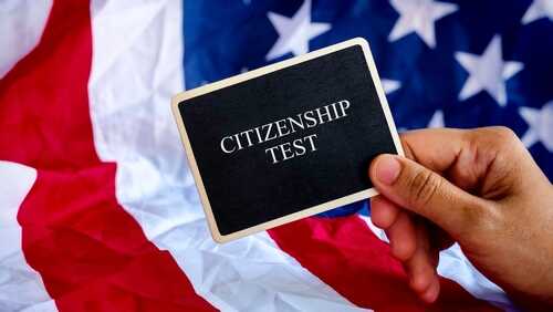 shutterstock_2632981605.jpg Hand holding a card that reads CITIZENSHIP TEST in front of an American flag