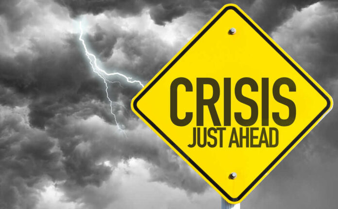 shutterstock_327481232.jpg Yellow sign reading Crisis Just Ahead with stormy sky
