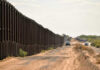 A long border wall stretching through a desert landscape with vehicles nearby