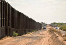 A long border wall stretching through a desert landscape with vehicles nearby