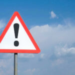 Triangle warning sign with exclamation mark against sky