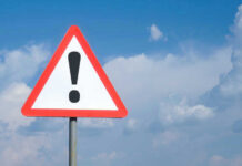 Triangle warning sign with exclamation mark against sky