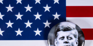 A black and white badge of John F. Kennedy on an American flag background