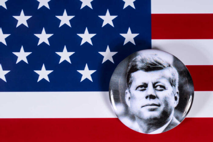 A black and white badge of John F. Kennedy on an American flag background