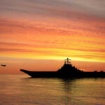 Silhouette of an aircraft carrier at sunset.