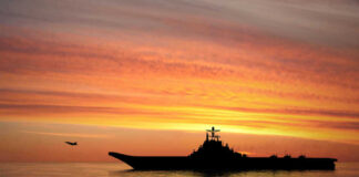 Silhouette of an aircraft carrier at sunset.
