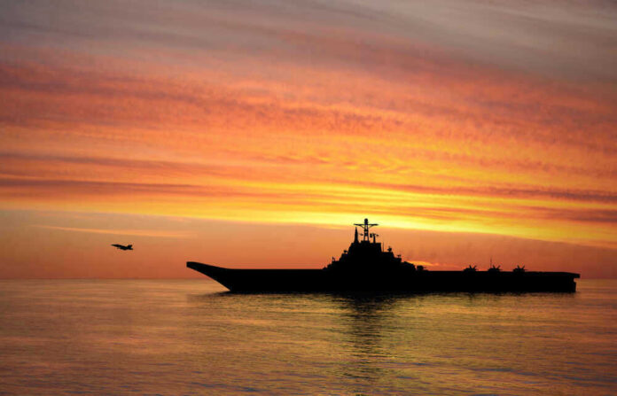 shutterstock_1449359894.jpg Silhouette of an aircraft carrier at sunset.