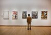 A person standing in an art gallery, observing various modern art pieces on the wall