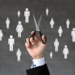 A hand holding scissors with icons of people in the background