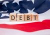 Wooden blocks spelling 'DEBT' on an American flag background