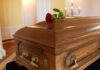 A wooden casket with a red rose placed on top