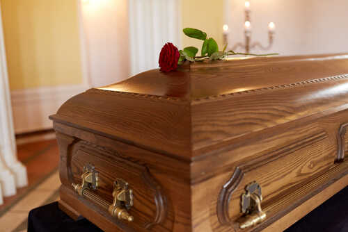 A wooden casket with a red rose placed on top