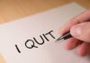 A hand writing 'I QUIT' on a piece of paper
