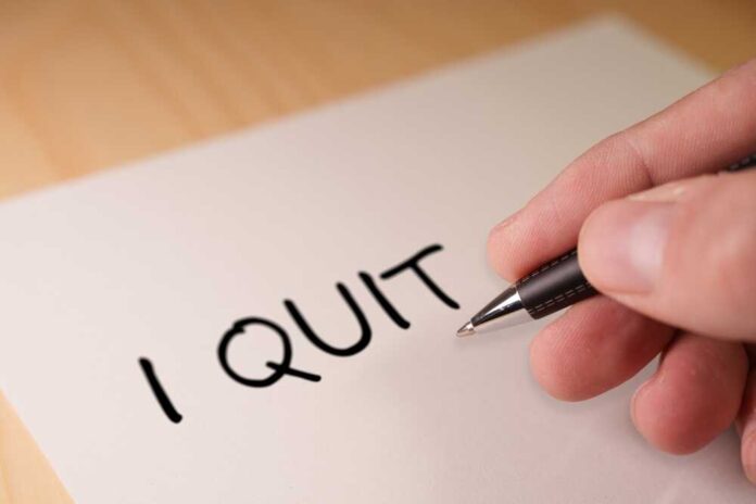 A hand writing 'I QUIT' on a piece of paper