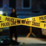 DEADLY TERROR at Church Funeral — Manhunt Underway Police tape marking a crime scene with blurred figures in the background