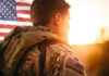 Soldier in uniform with American flag at sunset.