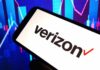 Verizon’s PATHETIC $20 Bribe Backfires Spectacularly A smartphone displaying the Verizon logo in front of a colorful stock market graph