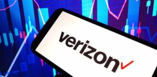 A smartphone displaying the Verizon logo in front of a colorful stock market graph