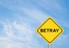 A yellow warning sign with the word 'BETRAY' against a blue sky