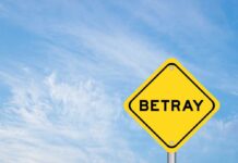 A yellow warning sign with the word 'BETRAY' against a blue sky