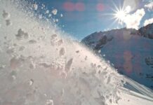 Snow spraying from a slope under a bright sun