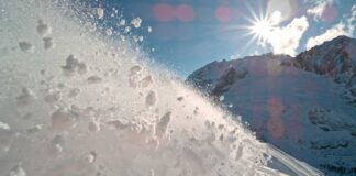 Snow spraying from a slope under a bright sun