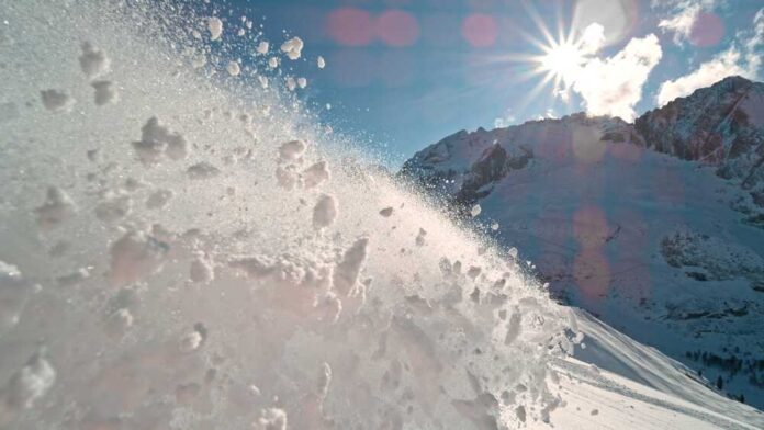 Snow spraying from a slope under a bright sun